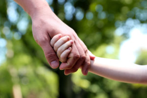A father holds the hand of a small child on a green background