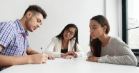 husband signing a document in front of wife and parenting coordinator at a table
