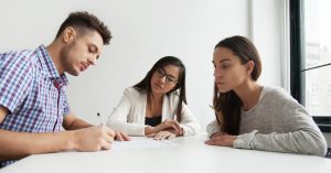 husband signing a document in front of wife and parenting coordinator at a table