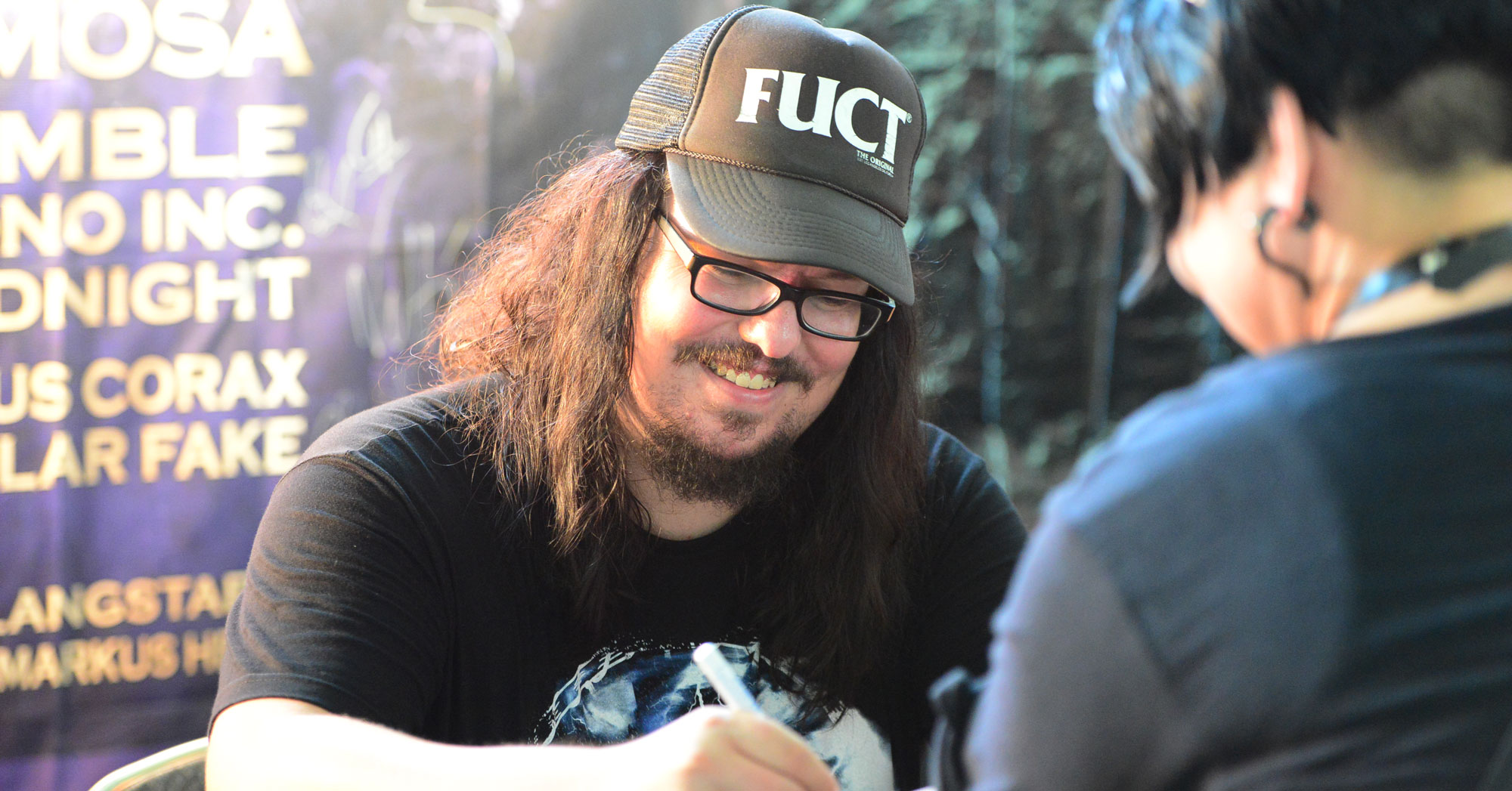 man signing autograph wearing a fuct brand streetwear clothing cap