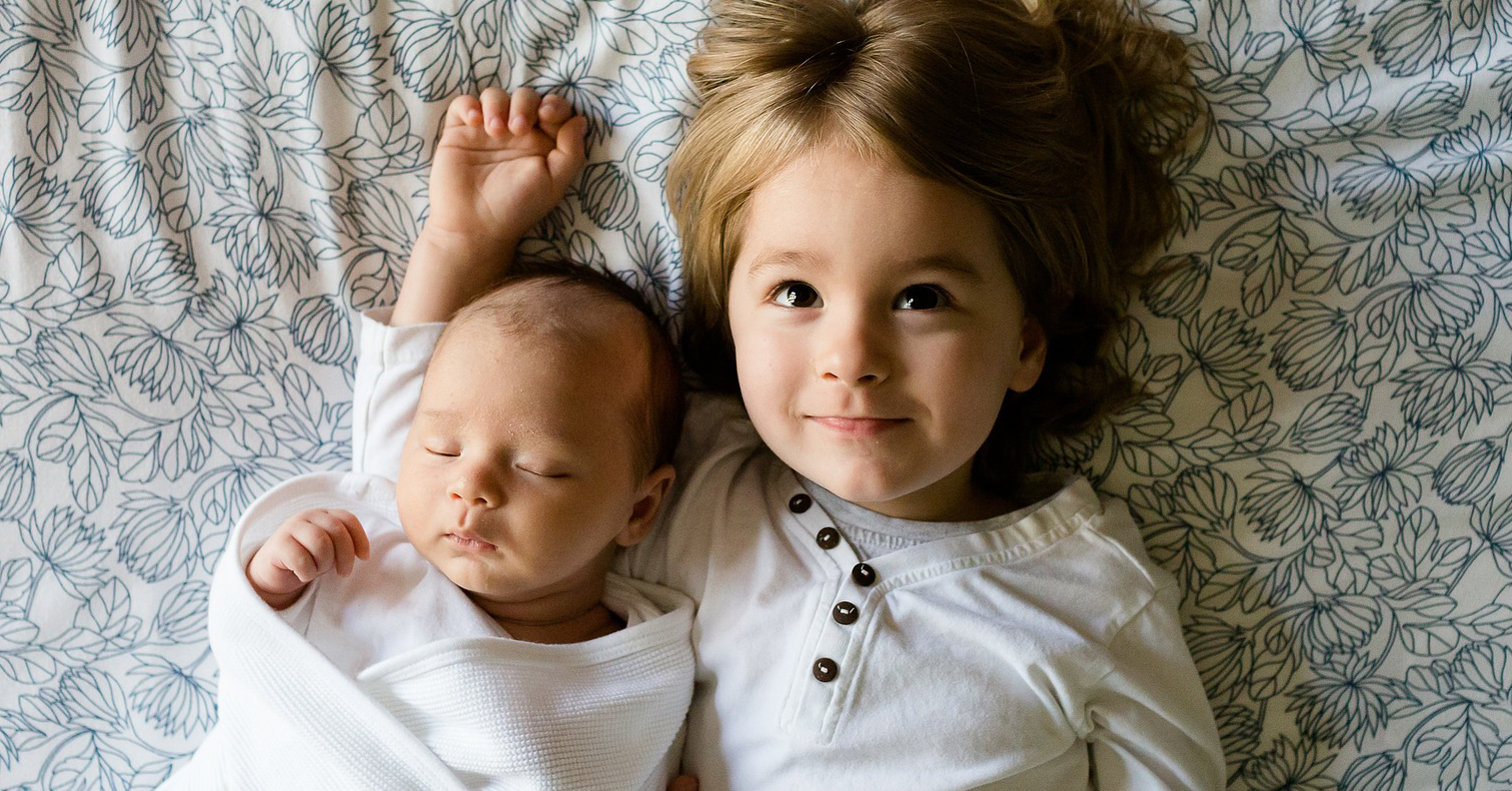 Child Tax Credit - Toddler and newborn brothers laying on a bed sleeping and smiling
