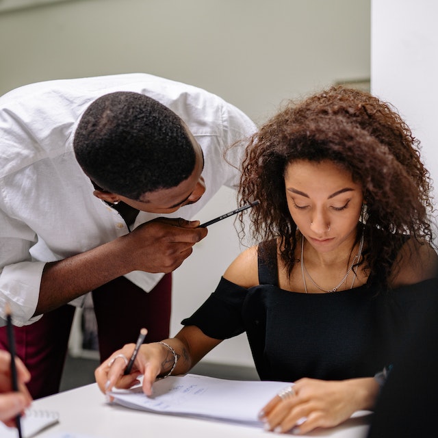 Man close to a woman coworker with a pencil in her face to demonstrate workplace harassment and potential need for an employment lawyer