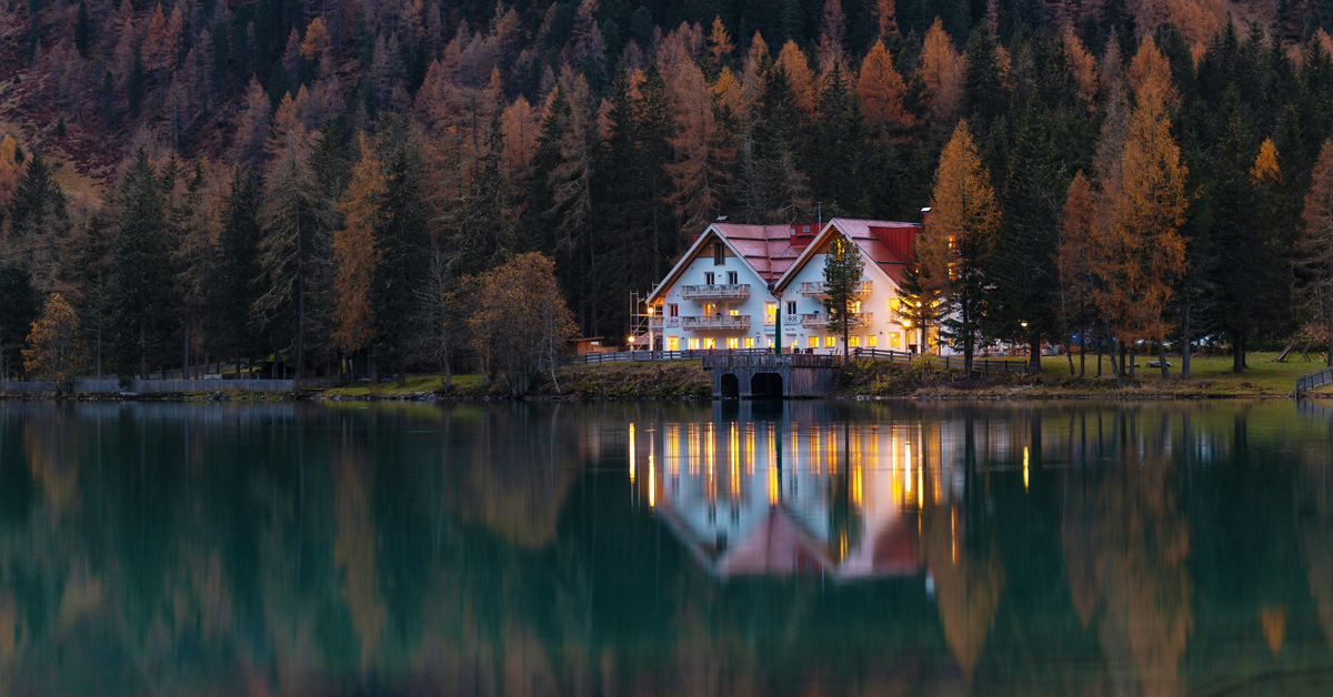 house on a lake at dusk in front of a mountain full of trees