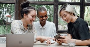 3 woman employees looking at a cell phone and laughing