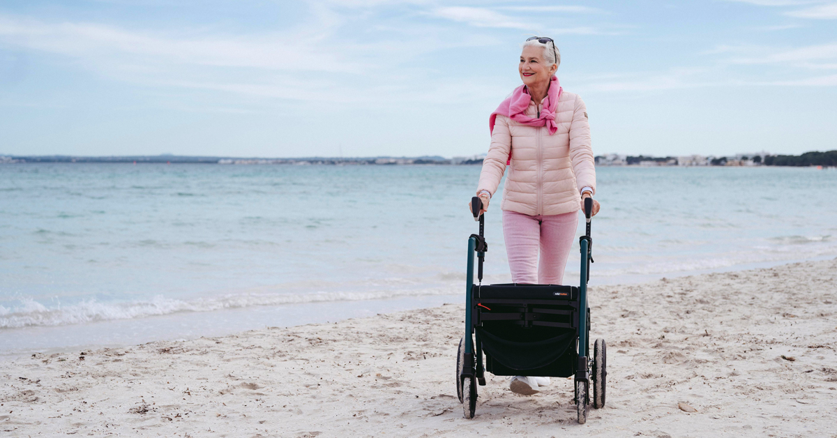 older woman with walker strolling the beach with a smile on her face after her gray divorce